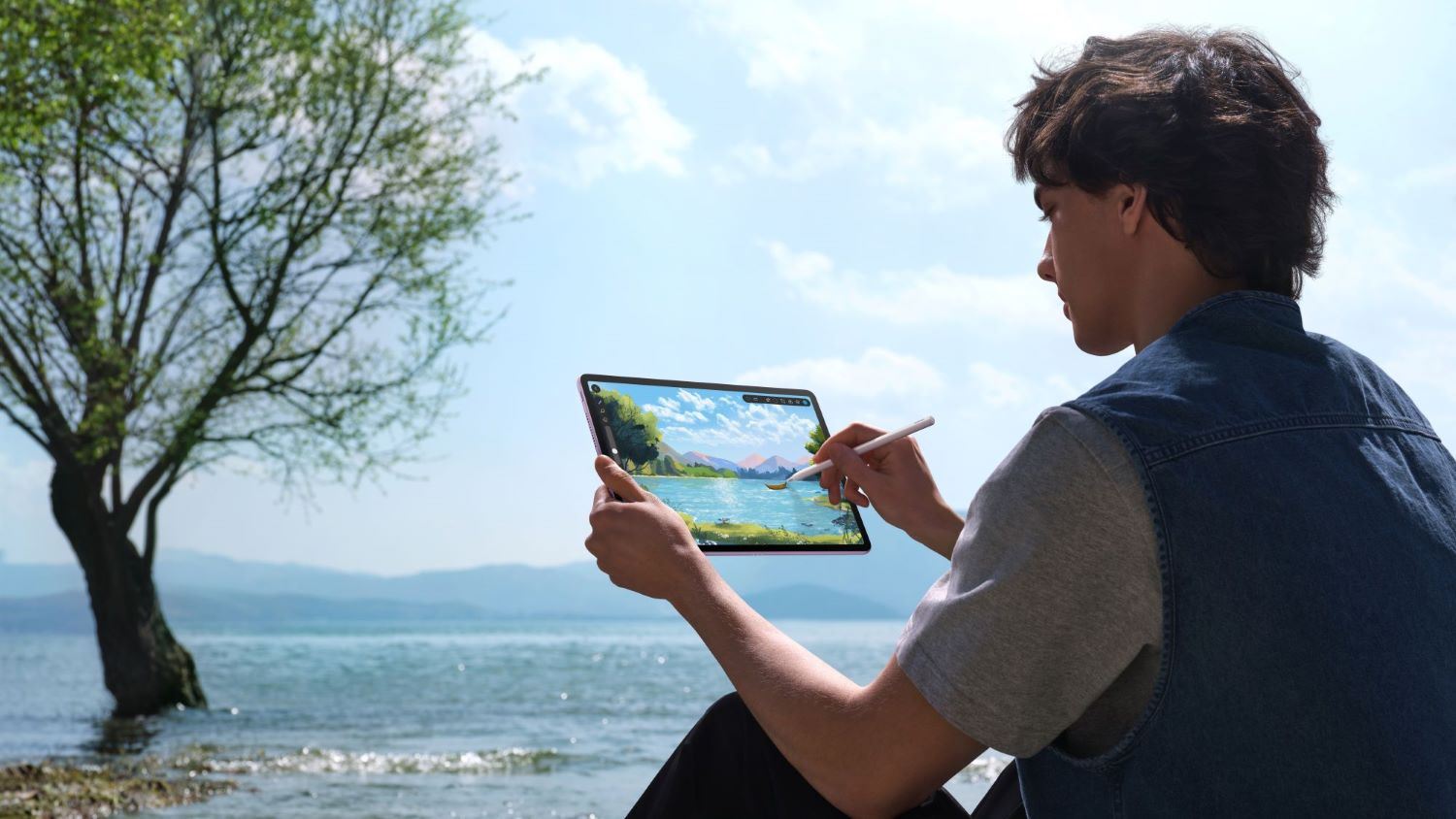 Young man sitting by the beach and painting a scenic view of tree and sea on his HUAWEI MatePad PaperMatte